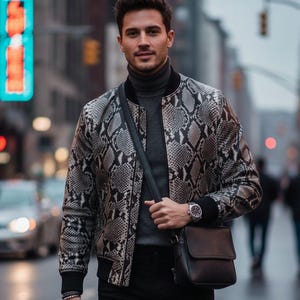 May include: A bomber jacket with a snakeskin pattern in shades of gray and black. The jacket has a black collar and cuffs. The person is wearing a gray turtleneck, black pants, a black leather crossbody bag, and a silver watch.
