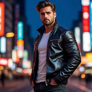 Könnte beinhalten: Schwarze Lederjacke mit Reißverschluss und weißem T-Shirt. Die Jacke hat ein klassisches Design mit Kragen und Taschen. Die Person trägt dunkelblaue Jeans. Der Hintergrund ist eine nächtliche Stadtstraße.