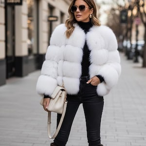 Puede incluir: Una mujer con una chaqueta de piel blanca, un cuello alto negro y vaqueros negros, sosteniendo un bolso crema con una cadena dorada. También lleva gafas de sol y botas marrones.