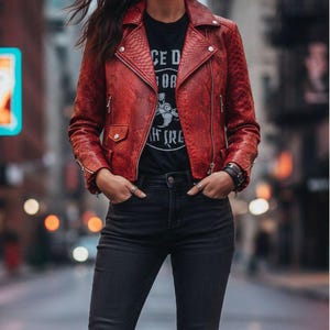 May include: A red snakeskin-effect biker jacket with silver zips and studs. The jacket is worn with a black graphic tee and dark wash jeans. The tee features the text "CE D OR" and a graphic.