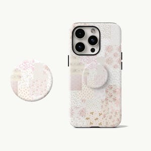 May include: A white phone case and matching phone grip with a patchwork design. The design features various floral and butterfly patterns in shades of pink, cream, and beige. The phone case has a built-in camera and flash.