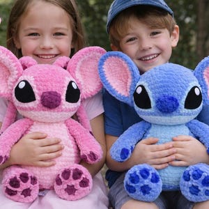 Puede incluir: Dos niños sonriendo, cada uno sosteniendo una gran muñeca de ganchillo. Una es rosa, la otra azul, ambas con orejas grandes y ojos negros. Las muñecas están basadas en un popular personaje de animación.