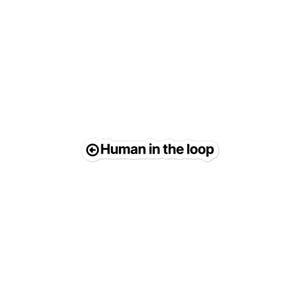 May include: A white die-cut sticker featuring the black text Human in the loop with a circular arrow icon pointing to the left placed before the text. The sticker has a clean, rounded rectangular shape with a thin white border around the lettering.
