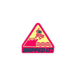 Pode incluir: Um adesivo triangular com fundo amarelo e borda rosa. Apresenta um pequeno robô saltando de um cais para águas onduladas, segurando uma caixa com um símbolo de código. O texto SHIPPED IT! está impresso em letras azul-escuras na parte inferior.