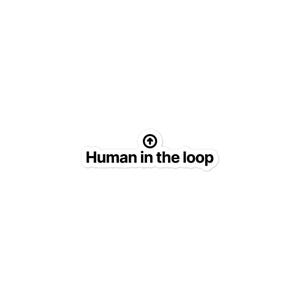 May include: A white die-cut sticker featuring the black text "Human in the loop" in a bold sans-serif font. Above the text is a small black circle containing a white upward-pointing arrow. The sticker has a clean, simple design.