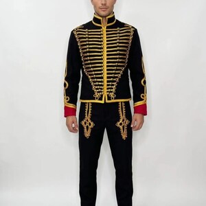 May include: A black military-style jacket and matching pants with gold embroidery and red accents. The jacket features a high collar and rows of gold braid. The pants have decorative gold designs near the pockets. The outfit is completed with black shoes.