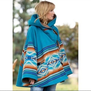 Puede incluir: Poncho con capucha turquesa con un estampado de inspiración suroeste en tonos naranja, azul y blanco. Cuenta con cierres de palanca de madera y forro marrón. El diseño incluye patrones geométricos y a rayas.