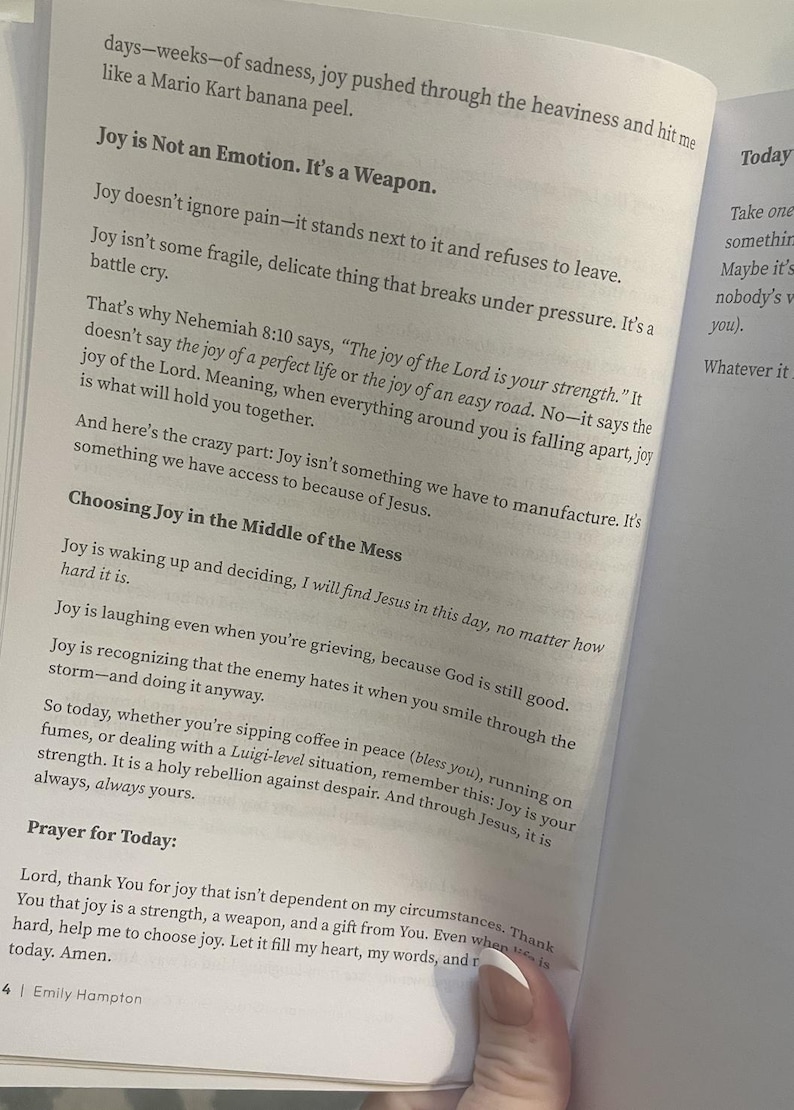 May include: Open book with text about joy, including the phrases "Joy is Not an Emotion. It's a Weapon" and "Choosing Joy in the Middle of the Mess." The pages are white with black text.