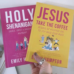 May include: Two books with colorful covers. One is pink with the title "HOLY SHENANIGAN" and the other is yellow with the title "JESUS TAKE THE COFFEE". Both books have illustrations and text. The books are held by a person.