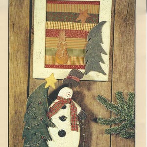 May include: A wooden snowman and tree Christmas decoration. The snowman has a wired-on hat and a red and green scarf. The tree is wrapped in a mini-light garland. The framed picture above has a star and a snowman.