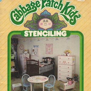 May include: A Cabbage Patch Kids Stenciling craft kit package featuring a yellow background with green text. The cover displays a nursery room with a crib, dresser, table, two chairs, and a cradle, all decorated with stenciled heart and doll motifs.
