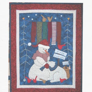 May include: A quilt pattern titled Free Scarves by Jenny Penny Designs, measuring 24.5 inches by 30 inches. The design features a snowman wearing a red hat and scarf, a polar bear, hanging scarves, and signs reading Free Scarves and Seed.