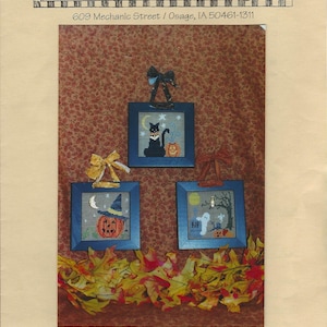 Peut inclure: Un modèle de broderie sur le thème d'Halloween avec trois motifs encadrés : un chat noir, une citrouille avec un chapeau de sorcière et un fantôme. Le texte "Waxing Moon Designs" et "Halloween Hang-Ups" sont visibles.