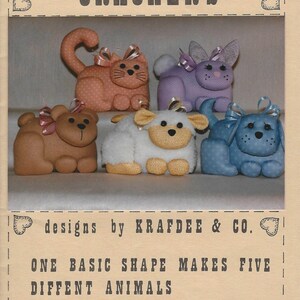Op de afbeelding: Een knutselpatroon met pluche dierencrackers. De afbeelding toont een kat, konijn, teddybeer, lam en puppy. Elk is ongeveer 10 cm hoog en 15 cm breed. De tekst luidt "Animal Crackers" en "designs by Krafdee & Co."