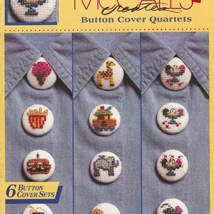 May include: A McCall's cross stitch kit for button cover quartets. The kit includes six sets of button covers with various embroidered designs, including a giraffe, elephant, and a lion. The text "16-Count Aida" is visible.