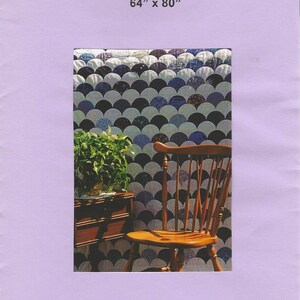 May include: A quilt with a clam shell pattern, measuring 64" x 80", is displayed. The quilt features a repeating design of semi-circles in shades of blue, white, and black. A wooden chair and a small wooden table with a plant are in the foreground.