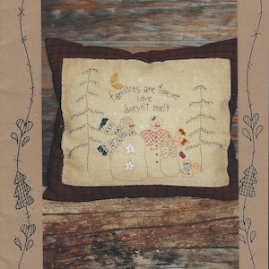 May include: A cushion with a rustic design, featuring embroidered snowmen and the phrase "families are forever love doesn't melt." The design is set against a plaid background, with the words "Love Doesn't Melt" and "Waltzing With Bears" at the top and bottom.