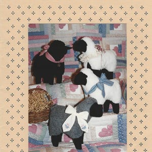Può includere: Un modello per il fai da te intitolato Wee Woolly 9" Sheep progettato da Anita Yoder. La copertina mostra quattro figure di pecore di peluche in nero, bianco e grigio, decorate con nastri e pizzo, su uno sfondo di trapunta patchwork con un cestino.