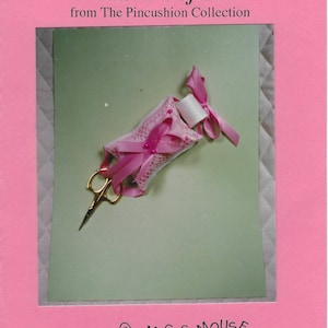 May include: A pink pincushion with lace detailing, a spool of thread, and gold scissors. The text "A Little Bit of Lace" and "Magic Mouse Creations" are visible. The image is set against a light green background within a pink frame.