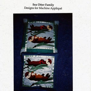 May include: Two square throw pillows with sea otter designs. The pillows feature a dark blue background with a green border and a detailed appliqué of otters resting on green seaweed. The text "WILD THINGS by Hot Yotts" is at the top.