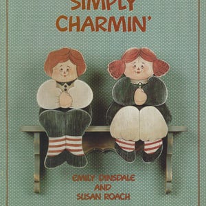 Puede incluir: Un adorno de pared de madera de estilo vintage con dos figuras pintadas, cada una con cabello rojo, atuendos negros y calcetines a rayas, sentadas en una pequeña repisa. Las palabras "SIMPLY CHARMIN'" están encima de las figuras, con los nombres "EMILY DINSDALE AND SUSAN ROACH" debajo.