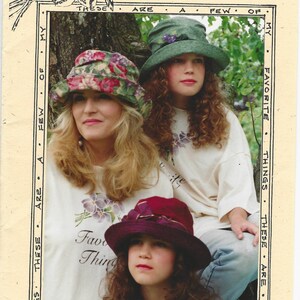 May include: A printed card featuring the text Favorite Things and Enchanted April, displaying three people wearing bucket hats in floral, solid green, and solid maroon colors. The people wear white shirts with floral graphics and the text Favorite Things.
