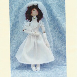 Puede incluir: Una muñeca de tela llamada Diana con un vestido de novia blanco, velo y guantes, con cabello oscuro y rizado. El texto dice Diana, An Elegant 18" doll y Hannily Patterns. La muñeca presenta un rostro sencillo con ojos pequeños y boca roja.