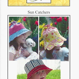 Op de afbeelding: Een Buttercup Quilts patroon getiteld Sun Catchers met drie bucket hats. Eén hoed is rood en blauw met sterren en ruiten, één is geel met roze cirkels, en één is blauw en wit gestreept met een rode rand. Elke hoed heeft een trekkoord.