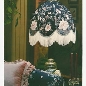 Puede incluir: Una pantalla de lámpara vintage con un estampado floral oscuro, flecos blancos y el texto "focal point Patterns". La imagen también muestra una almohada, velas y un tarro de cristal. El texto "#4005 SOUTHERN SERENITY" también es visible.