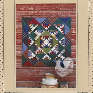 May include: A pattern booklet titled Quilter's Coop #113 Mountains and Meadows featuring a square quilt with a geometric star design in shades of green, blue, red, and white, displayed against a red wooden wall with a metal milk can and rooster.
