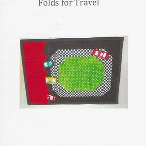 Könnte beinhalten: Eine Rennstrecken-Tischset mit schwarzem Rand, rotem Abschnitt, grünem Zentrum und Schachbrettmuster. Das Tischset hat Spielzeugautos darauf. Der Text "RACETRACK PLACEMAT Folds for Travel" steht oben.