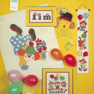 May include: A yellow background features a cross-stitch pattern of clowns, balloons, and the text "Just Clownin' Around." The image includes framed cross-stitch pieces with the name "Jennifer" and the word "I'm."