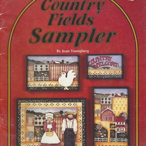 Könnte beinhalten: Ein roter Einband mit dem Titel "Country Fields Sampler" und Kunstwerken von Landszenen. Die Kunstwerke umfassen einen Hahn, ein Paar und verschiedene Bauernhofgebäude. Der Einband hat einen gelben Rand.