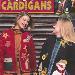 Peut inclure: La couverture du livre "Christmas Cardigans" présente deux femmes portant des cardigans appliqués festifs. L'un est rouge avec des motifs de Noël, l'autre noir avec des tournesols et un bonhomme de neige. La couverture comprend également une petite image encadrée et le texte "6 Designs."