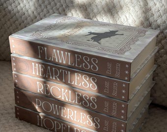 May include: A stack of five hardcover books with brown spines and light-colored covers. The titles read "Flawless," "Heartless," "Reckless," "Powerless," and "Hopeless." Each spine features the author's name, "Elsie Silver." The covers have a decorative border and a silhouette.