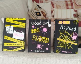 May include: Three books with black covers are displayed. The first book has yellow tape that reads "DO NOT CROSS" and the title "A Good Girl's Guide to Murder." The second book is titled "Good Girl, Bad Blood." The third book is titled "As Good As Dead."