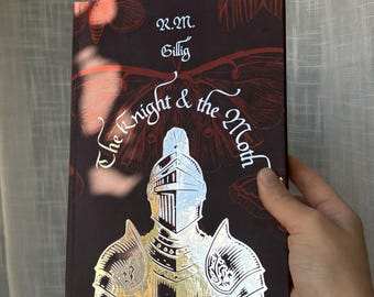 May include: A hardcover book titled "The Knight & the Moth" by R.M. Gillig. The cover is dark brown with a gold foil illustration of a knight in armor. The title and author's name are in white script. The background features a moth and leaf design.