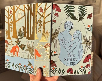 May include: A book with a light blue cover featuring a forest scene with gold trees, red mushrooms, and a fox. The title "THE STOLEN HEIR" is displayed with an illustration of two figures.