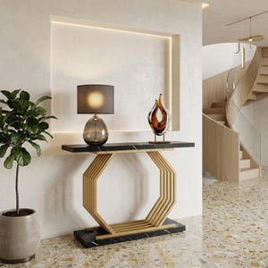 May include: A console table with a black marble top and base, featuring a gold-toned octagonal metal frame. On the table sits a dark glass lamp with a cylindrical shade and a flame-shaped amber glass sculpture. A potted plant stands nearby.