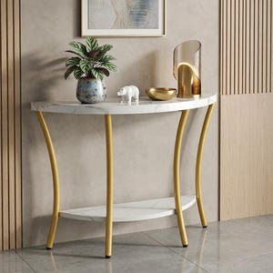 May include: A semi-circular console table featuring a white faux marble top and lower shelf supported by four curved gold metal legs. On the table sits a potted green plant, a small white bear figurine, a gold bowl, and a gold arched table lamp.