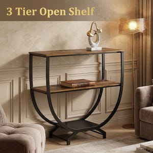 Può includere: Uno scaffale aperto a 3 livelli con finitura effetto legno marrone scuro e telaio in metallo nero. L'unità presenta una base curva semicircolare con tre superfici orizzontali. Un libro è appoggiato sul ripiano centrale del mobile.