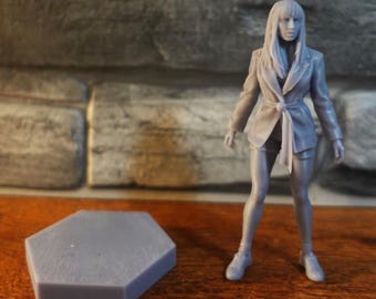 May include: A grey 3D printed miniature figurine of a person with long hair, wearing a belted blazer and shorts, standing next to a separate grey hexagonal base. The figure has a smooth, monochromatic finish and stands in an upright position.