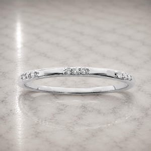 May include: A thin silver-toned metal band ring featuring three distinct clusters of small, clear, sparkling stones embedded along the top half of the band. The ring has a polished, reflective finish and a smooth, rounded profile throughout its design.