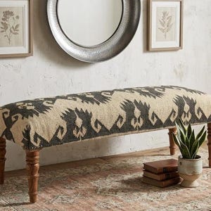 May include: A rectangular bench featuring a cream and charcoal gray patterned textile upholstery. The seat is supported by four turned wooden legs in a medium brown finish. The upholstery displays a repeating geometric motif across the top.