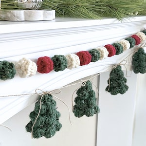 May include: A festive garland featuring alternating red, dark green, and cream-colored crocheted spheres strung together, accented with dangling, textured dark green crocheted pine tree shapes tied with thin, light brown twine bows.