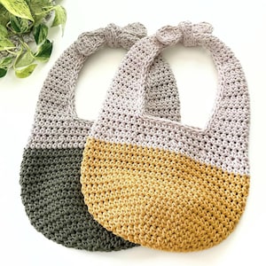 Peut inclure: Deux bavoirs pour bébé en crochet avec un design bicolore. L'un associe le gris clair au vert olive foncé, tandis que l'autre associe le gris clair au jaune moutarde. Les deux bavoirs ont une forme arrondie et un petit nœud sur le dessus.
