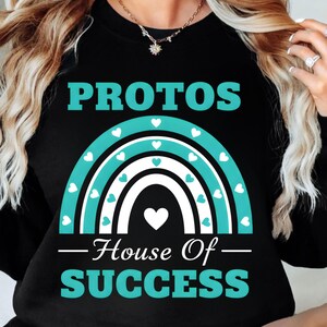 以下が含まれることがあります： 「PROTOS」の文字がプリントされた黒いスウェットシャツ。ターコイズと白の虹のデザインで、ハートのアクセントが付いています。虹の下には「House Of SUCCESS」の文字。カジュアルなスタイルの衣服です。