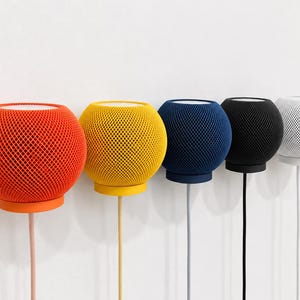 May include: A row of five spherical smart speakers with a mesh fabric exterior, each featuring a flat top surface and a circular base. The speakers are arranged in a line, displaying colors of orange, yellow, blue, black, and white, with power cords.