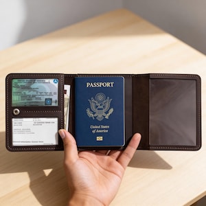 May include: A brown leather passport holder with a blue United States passport inside. The holder is open, revealing slots for a driver's license and other cards. The holder is on a wooden surface.