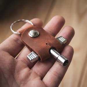 May include: A brown leather keychain with a silver key ring and a metal multi-tool. The leather case has a snap closure and holds several metal attachments. The multi-tool includes a socket and charging ports.